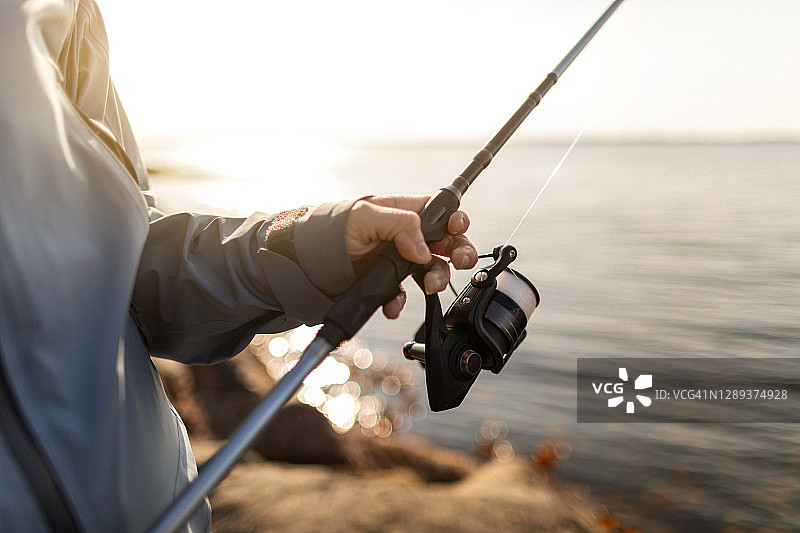 男人在海边的岩石上用钓竿钓鱼图片素材