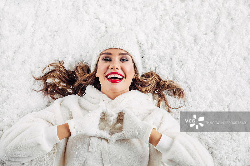 女孩躺在雪地上，比出爱心图片素材