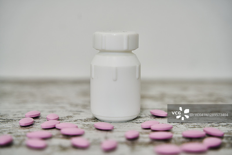 装有药物的白色药瓶，药丸散落在桌子上图片素材