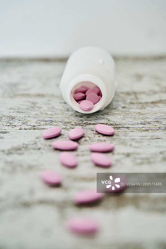 装有粉色药丸的白色医药容器，散落在桌子上图片素材