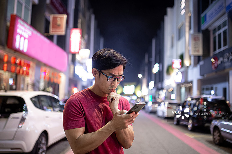 夜晚街头面露担忧之色的中国男子正在看手机图片素材