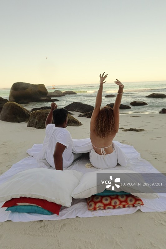 黎明时分，情侣在沙滩上亚麻床上用品中醒来，她正在伸展身体图片素材