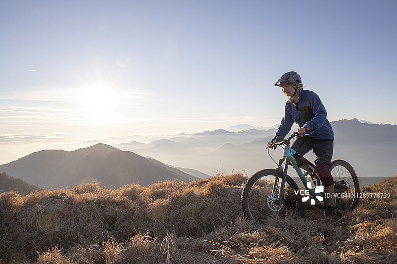 日出时分，年轻女子在山脊上骑山地自行车图片素材