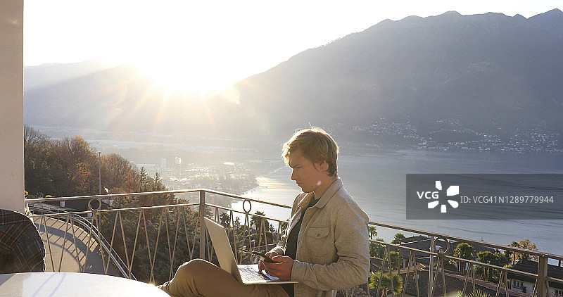 在公寓阳台上日出时用电脑工作的年轻人图片素材