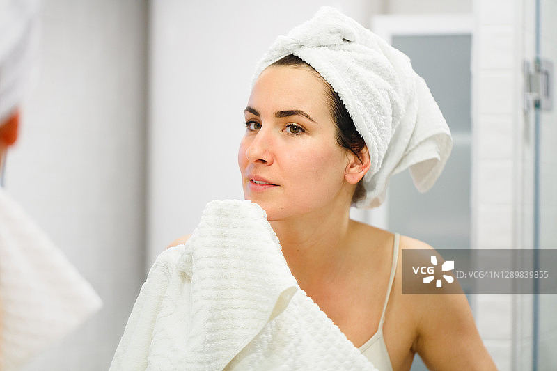 在镜子前用毛巾擦脸、头上裹着毛巾的女人图片素材