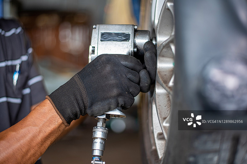 汽车修理工在修理厂更换白色汽车轮胎，修理工用螺母机拆卸轮胎图片素材