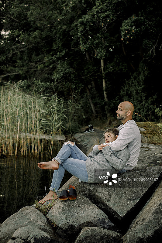 父女坐在湖边岩石上, 眺望远方图片素材