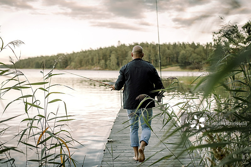 日落时分，男子在湖边码头手持钓竿的背影图片素材