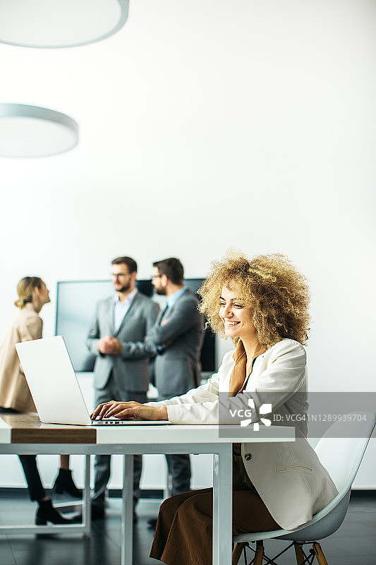 年轻女CEO在现代办公室工作，同事在后台讨论图片素材