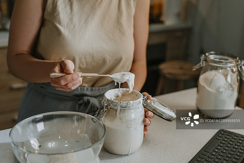 家庭爱好：一位匿名女性通过将活性酵母加入碗中，从头开始烘烤酸面包图片素材
