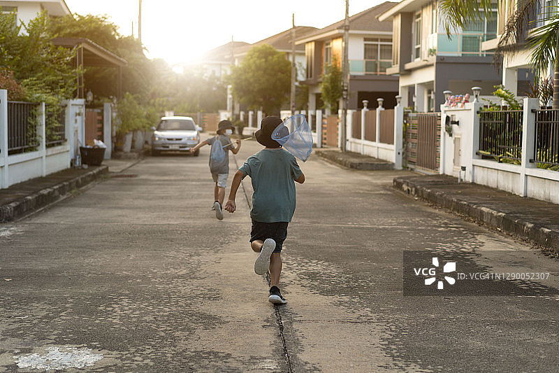 亚洲小男孩在阳光明媚的草地上用网兜捉蝴蝶，探索大自然的乐趣图片素材