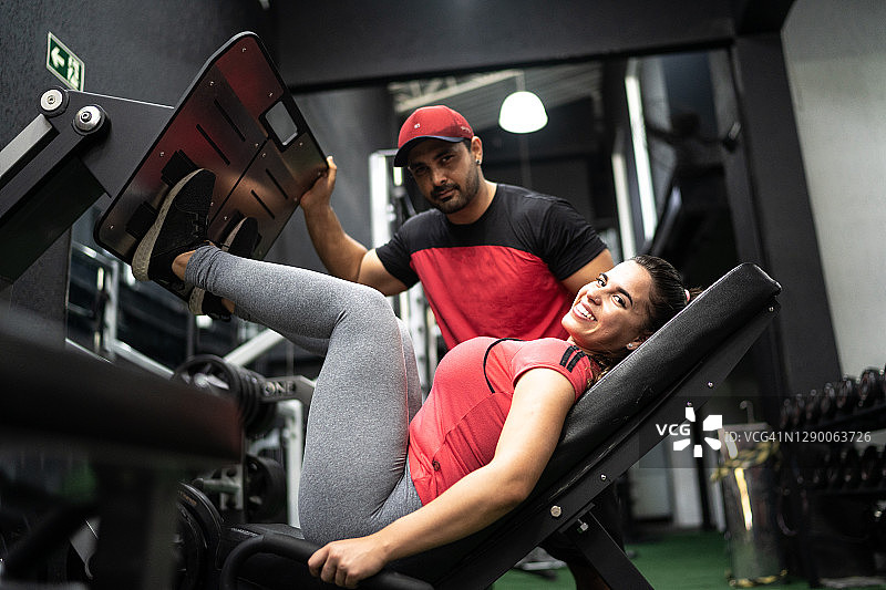 年轻女子在教练的帮助下进行腿部推举图片素材