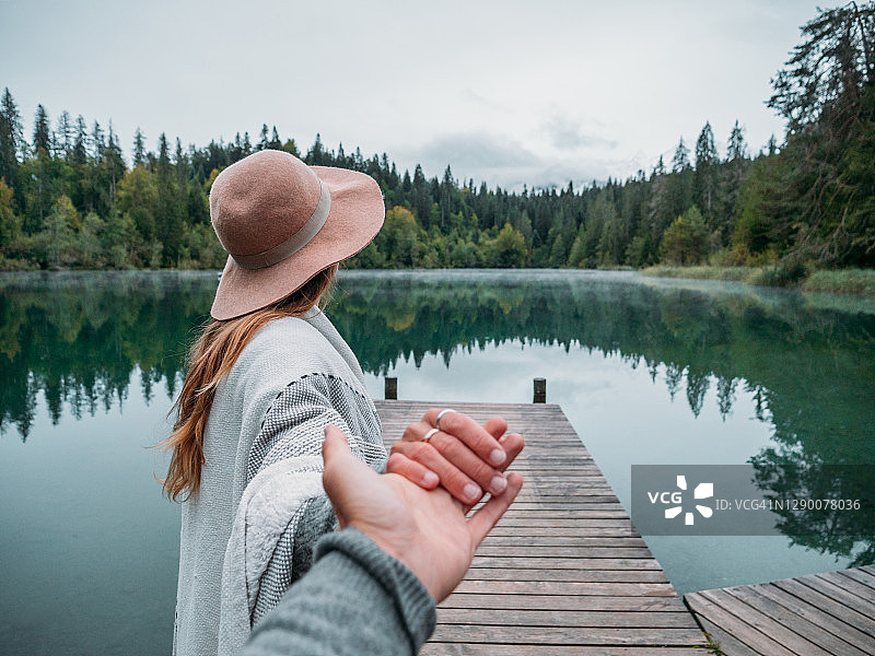 引领男友走上高山湖木制码头的女人图片素材