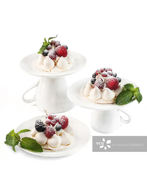 帕芙洛娃蛋白迷你蛋糕静物美食摄影，瓷盘装新鲜浆果薄荷，糖粉覆盖白色背景特写侧视图图片素材