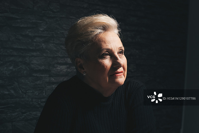坐着，向前看的年长金发女性。黑色背景特写图片素材