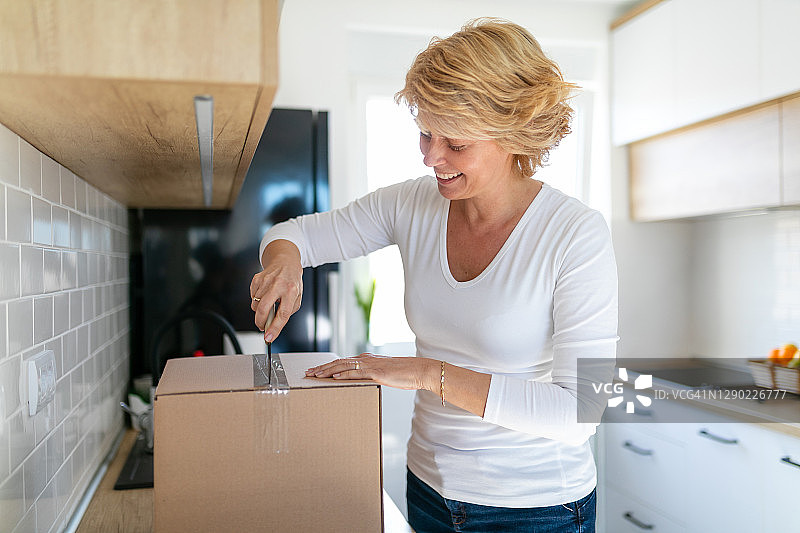 微笑的女人用厨房刀打开纸箱图片素材