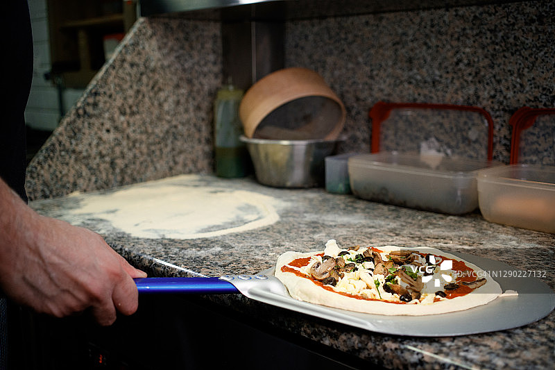 从厨房台面上用铲子拿起准备烘烤的披萨图片素材