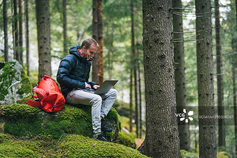 年轻男人在茂密的森林里远程工作图片素材