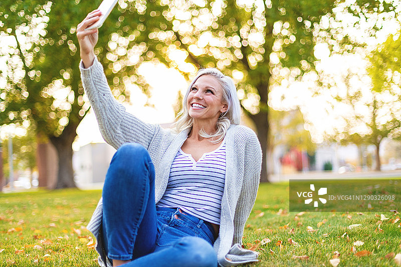 在公园里使用智能手机拍摄的有魅力的千禧一代女性照片图片素材