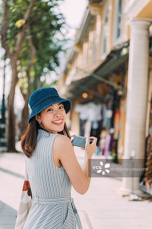 东南亚女游客在泰国曼谷考山路步行街用手机拍照并上传到社交媒体图片素材