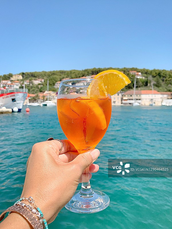 手持一杯阿佩罗鸡尾酒，背景是亚得里亚海和晴朗的蓝天特写图片素材