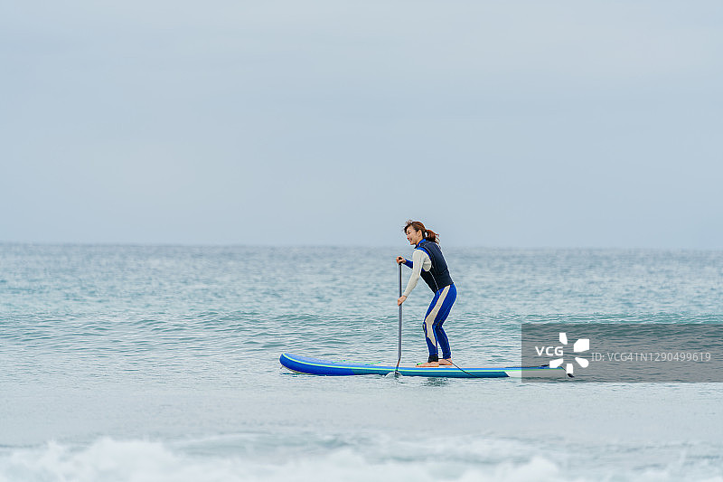冬天，女人穿着潜水服在海中划桨板图片素材