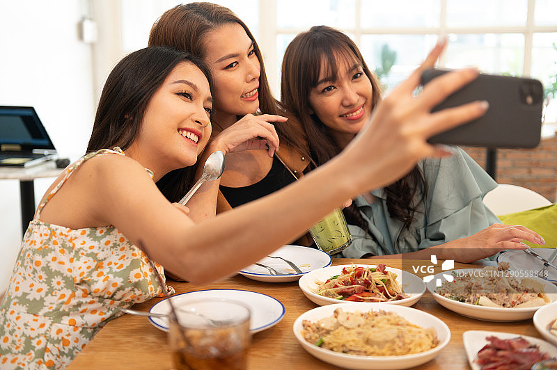一群亚洲年轻女性和朋友在传统泰国餐厅一起吃泰国菜时，用智能手机自拍图片素材
