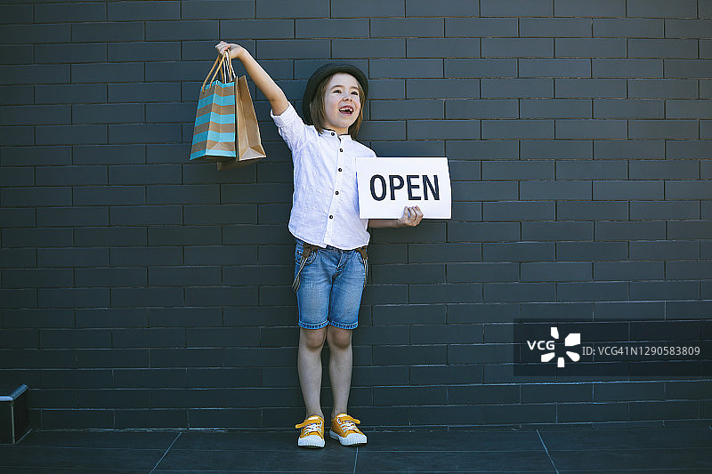 拿着“Open”标志和购物袋的快乐男孩图片素材