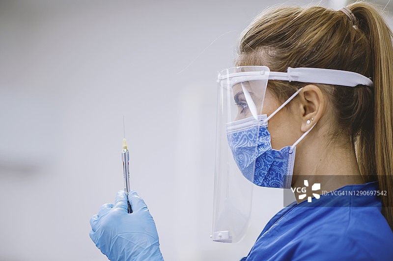 穿着防护服的女医生用注射器从药瓶中抽取疫苗液体图片素材