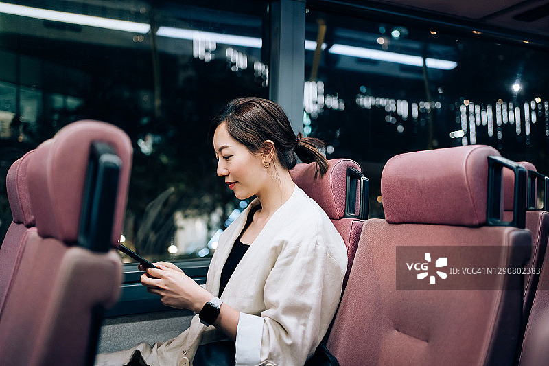 在公交车上使用智能手机的年轻亚洲女性图片素材