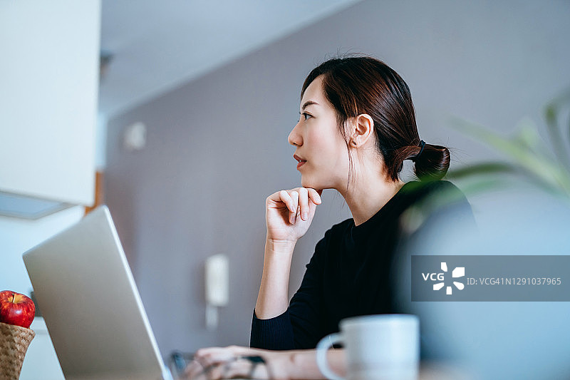 在家用笔记本电脑工作的沉思亚洲年轻女人图片素材