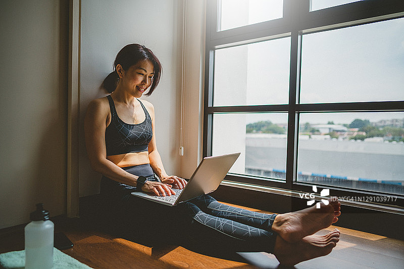 亚洲女性在客厅锻炼后使用笔记本电脑图片素材