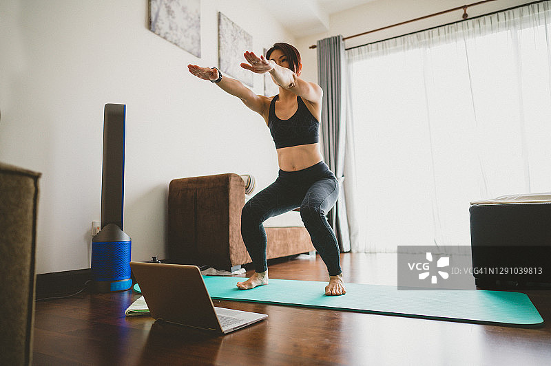 亚洲女性在室内笔记本电脑旁边的健身垫上做运动图片素材