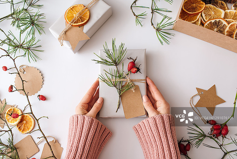 包装圣诞礼物。女人在白色背景上拿着手工制作的礼物。平铺，顶视图，复制空间。圣诞快乐，新年节日概念。图片素材