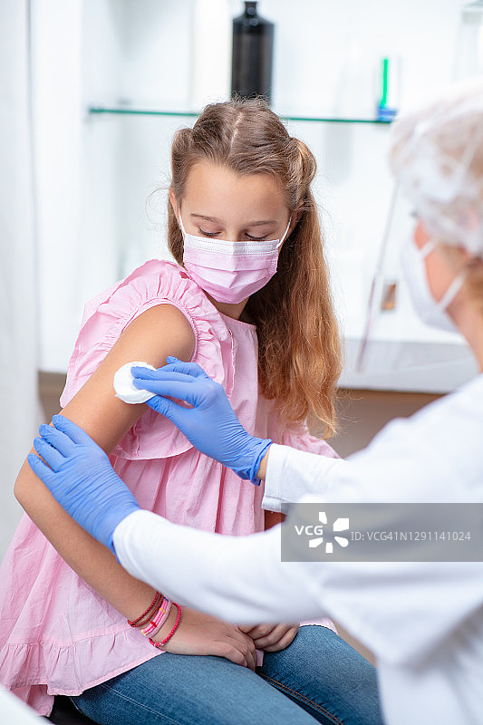 戴着防护口罩的女孩看着正在消毒准备接种疫苗的手臂图片素材