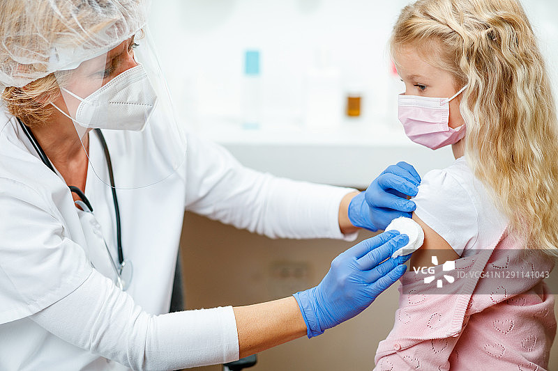 穿防护服的女医生为女孩手臂消毒准备接种疫苗图片素材