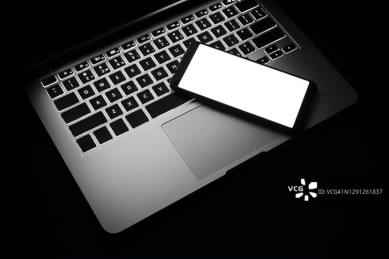 黑色背景中带白色屏幕的笔记本电脑和智能手机图片素材