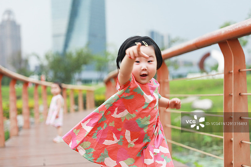 中国小女孩向我们跑来，她的姐姐在公园水池上的小路上图片素材