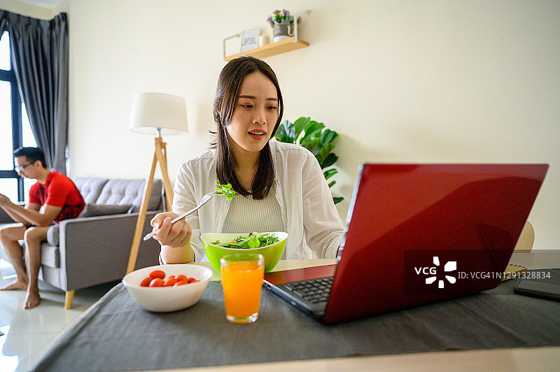 在家中客厅使用笔记本电脑享用健康食品的年轻亚洲女性图片素材