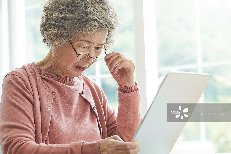一位视力不好的老妇人试图在平板电脑上看东西图片素材