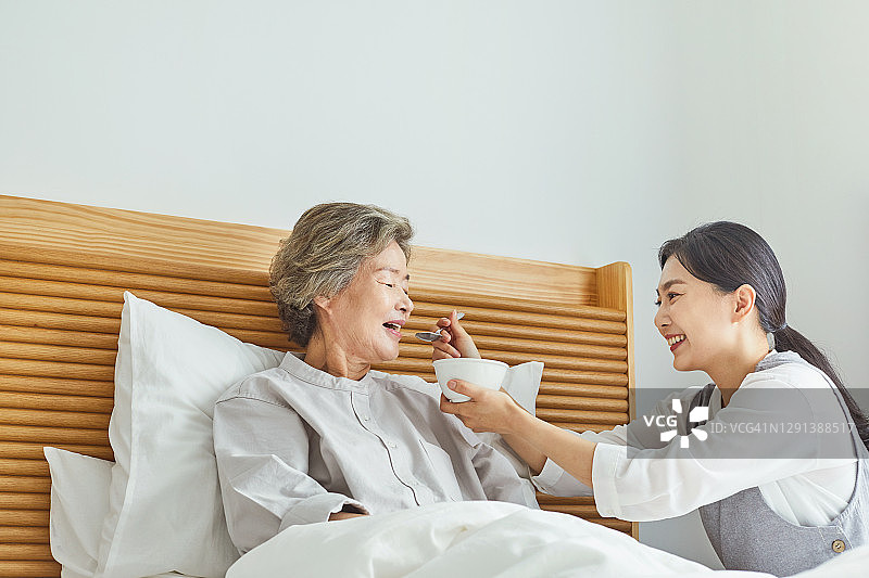 微笑的护士在床上喂食老年妇女图片素材