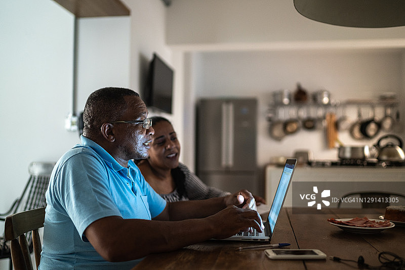 在家工作，使用笔记本电脑，妻子在他身边的老年男人图片素材