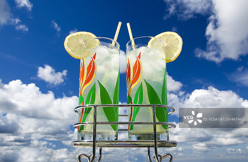 两个20世纪50年代复古柠檬鸡尾酒杯，带支架，位于室外露台上，上方是广阔的天空和云彩图片素材