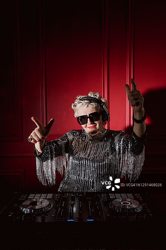 戴着耳机在DJ台前播放音乐和跳舞的老年妇女图片素材