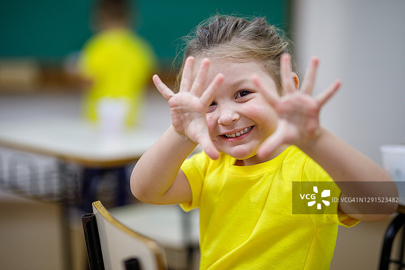 在教室里微笑的小女孩展示着他的手，看着镜头图片素材