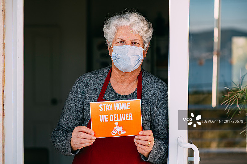 疫情期间佩戴口罩的女咖啡馆店主举着“居家外卖”标牌图片素材