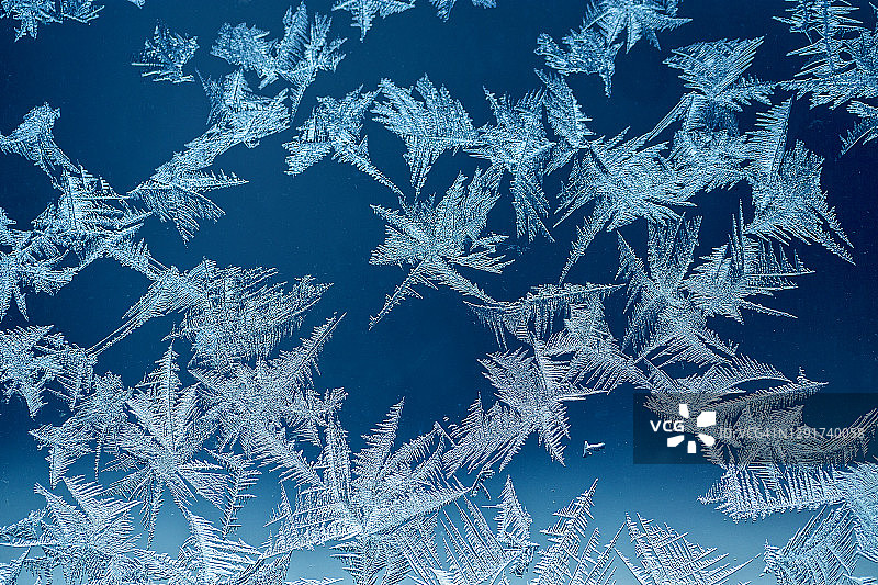 冬季冰冻深蓝色背景，窗户上的抽象霜花图案图片素材