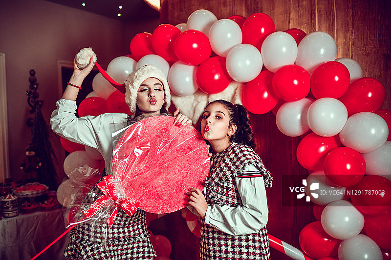 姐妹拿着巨型棒棒糖在圣诞气球前撅嘴图片素材