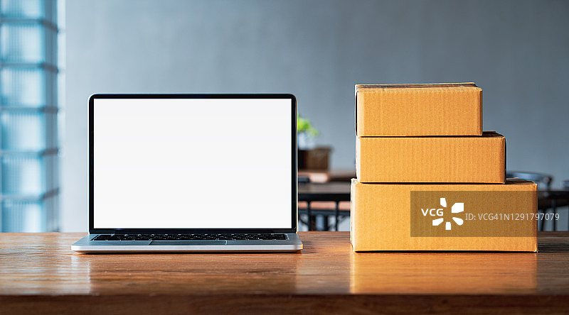 创业小企业主在工作场所使用笔记本电脑，纸板箱包裹产品准备交付给客户，在线销售，电子商务，在线购物，打包概念图片素材