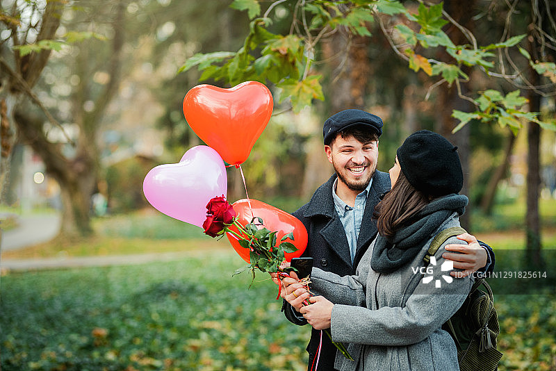 年轻男子用玫瑰花束和气球给女友惊喜照片。约会/爱情/情人节概念。图片素材